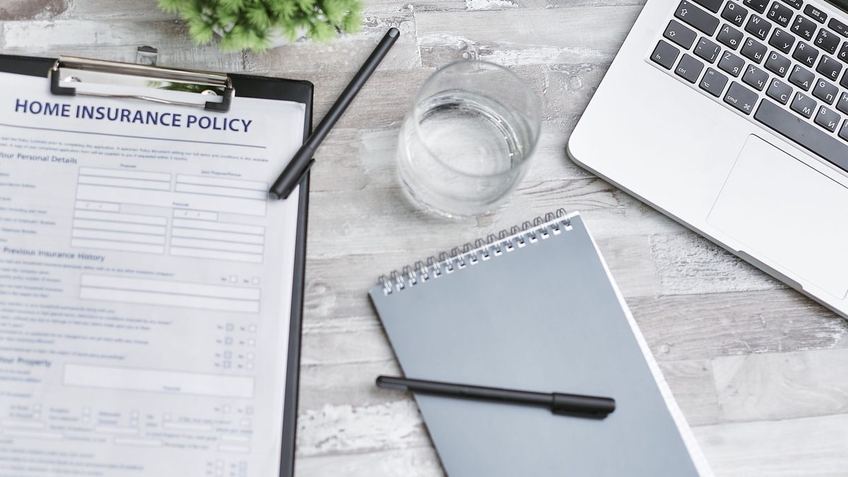 A home insurance policy document on a desk beside a laptop and notebook