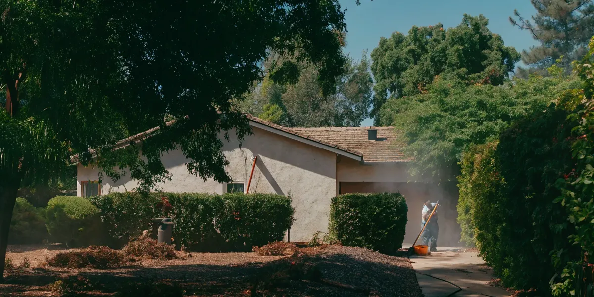 A person prepares their home for fire season by clearing brush to create defensible space.