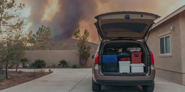 Car packed with emergency supplies for a wildfire evacuation with smoke in the background.